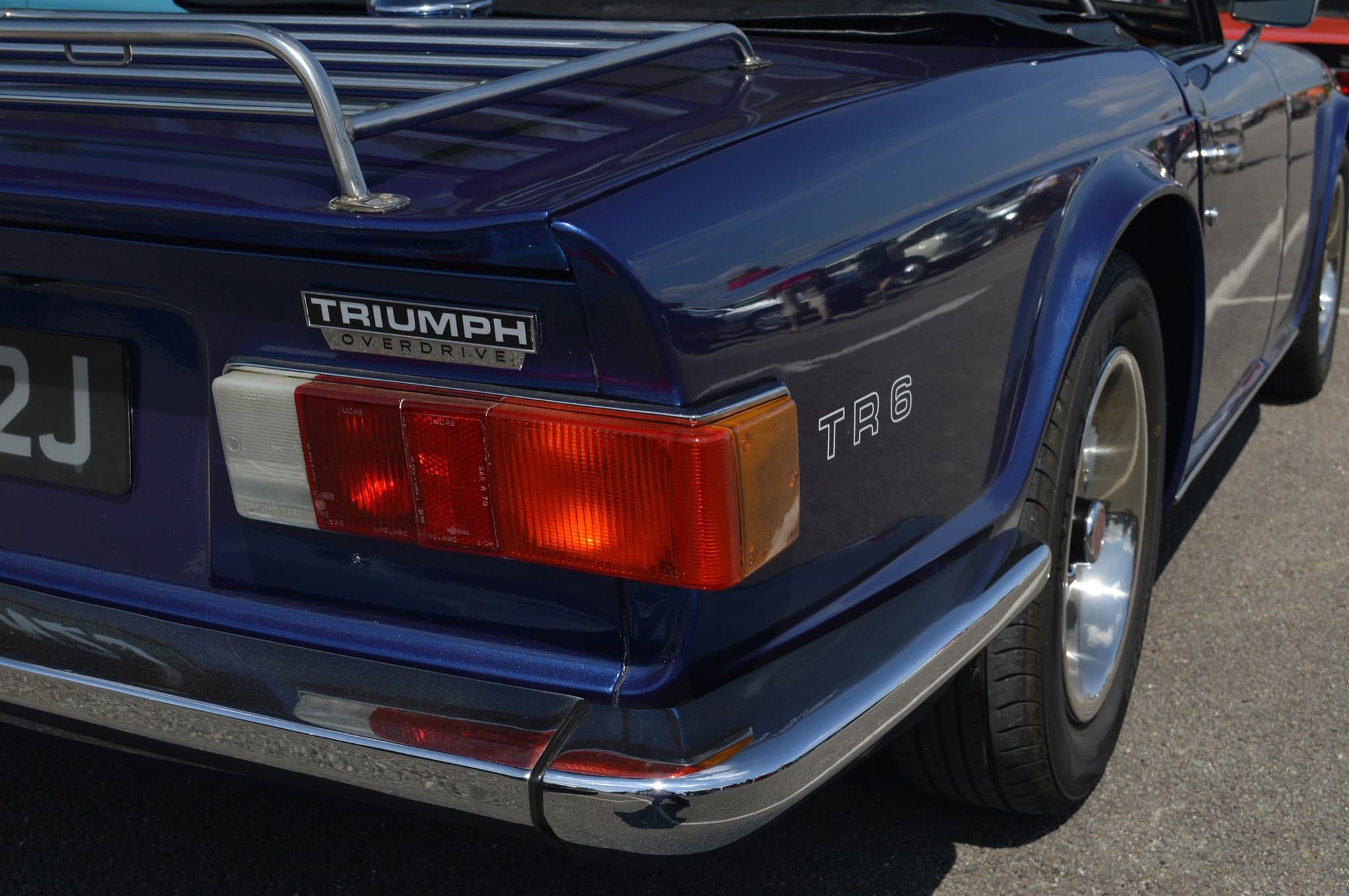 The tail of a dark blue Triumph TR6 with a TRIUMPH badge over the word OVERDRIVE, a luggage rack and a wrap-round tail lamp.