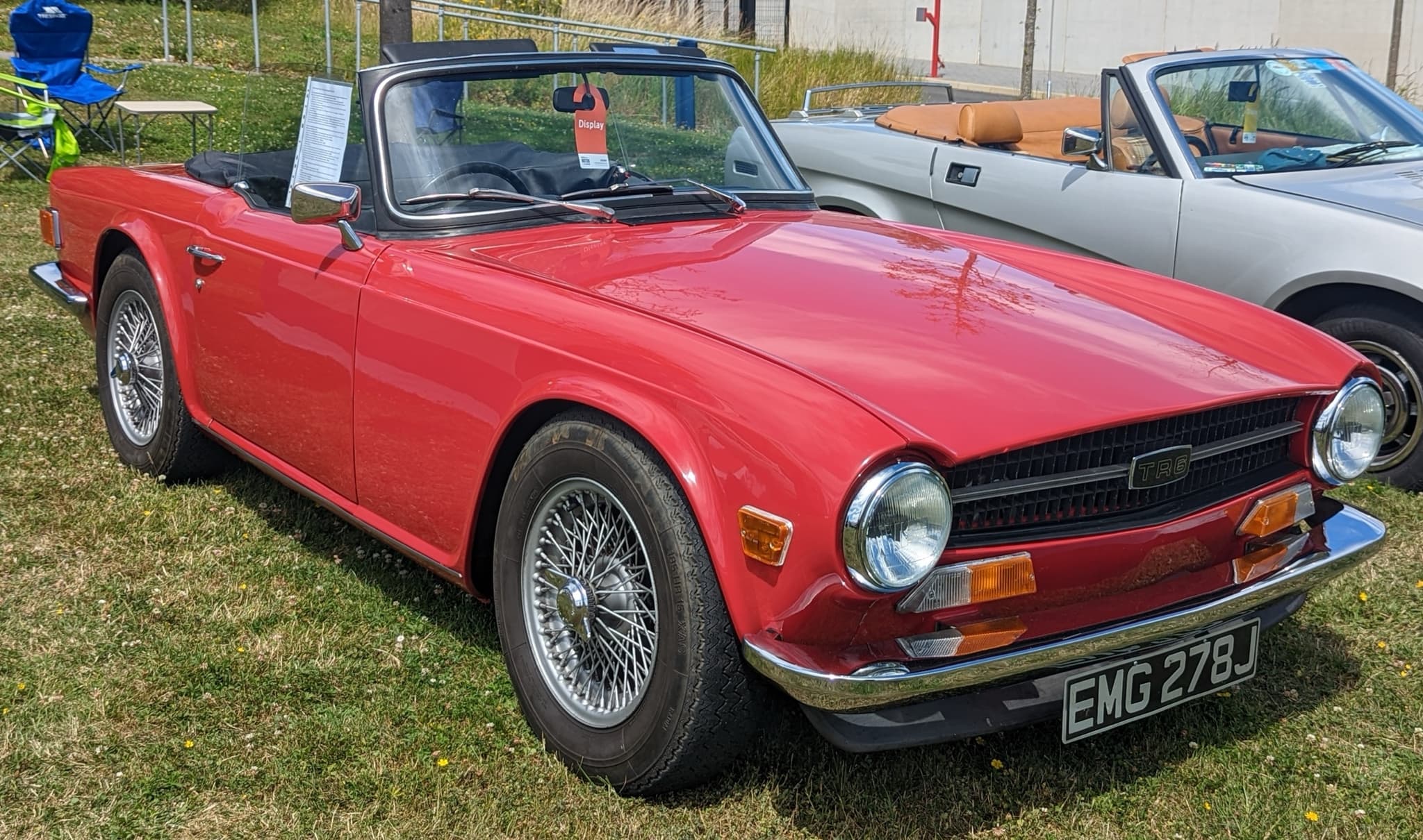 A red Triumph TR6 with wire wheels and the hood folded, on dry grass at a car show.