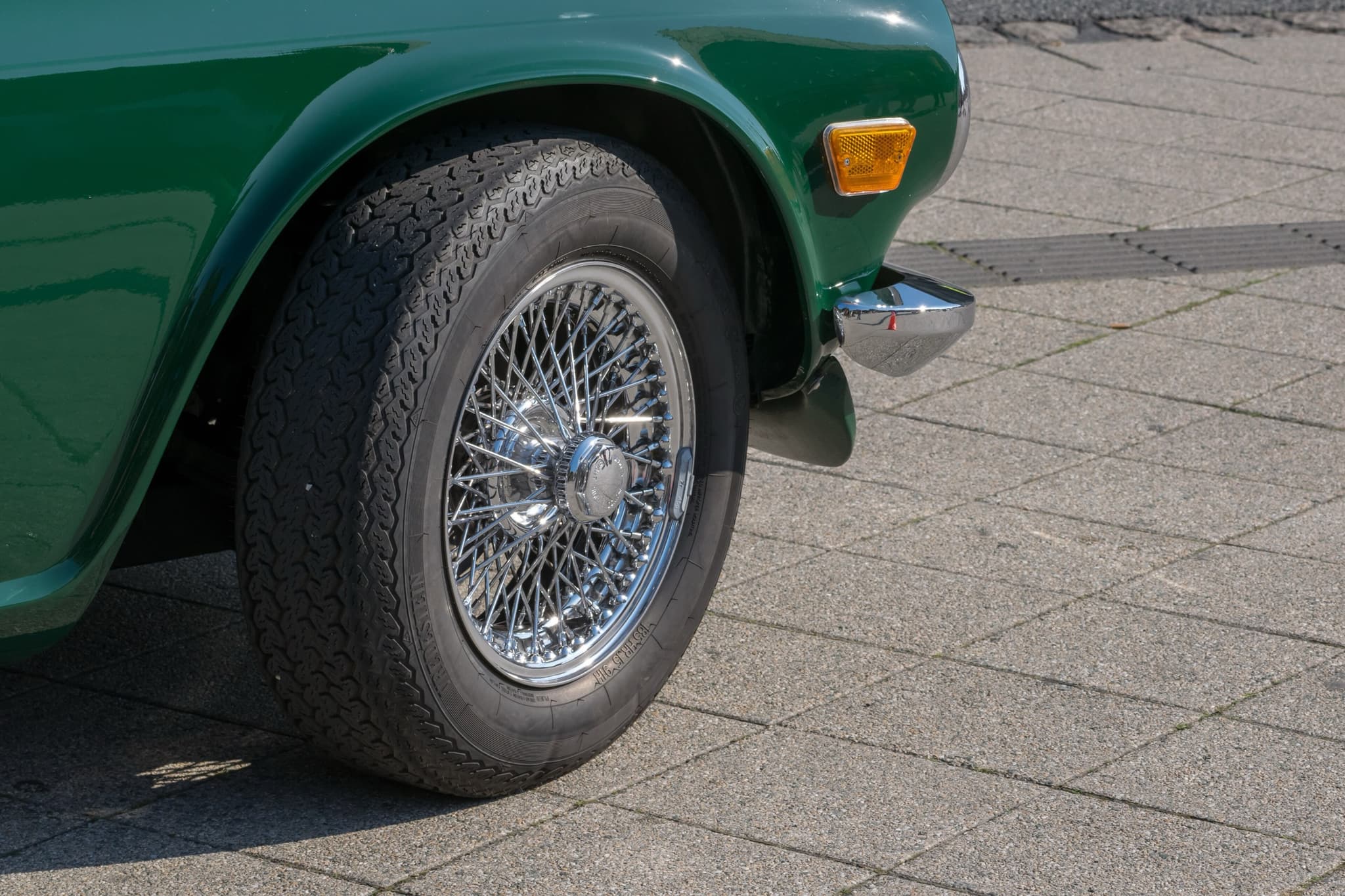A chrome wire wheel with a knock-off spinner on the front of a dark green Triumph TR6.