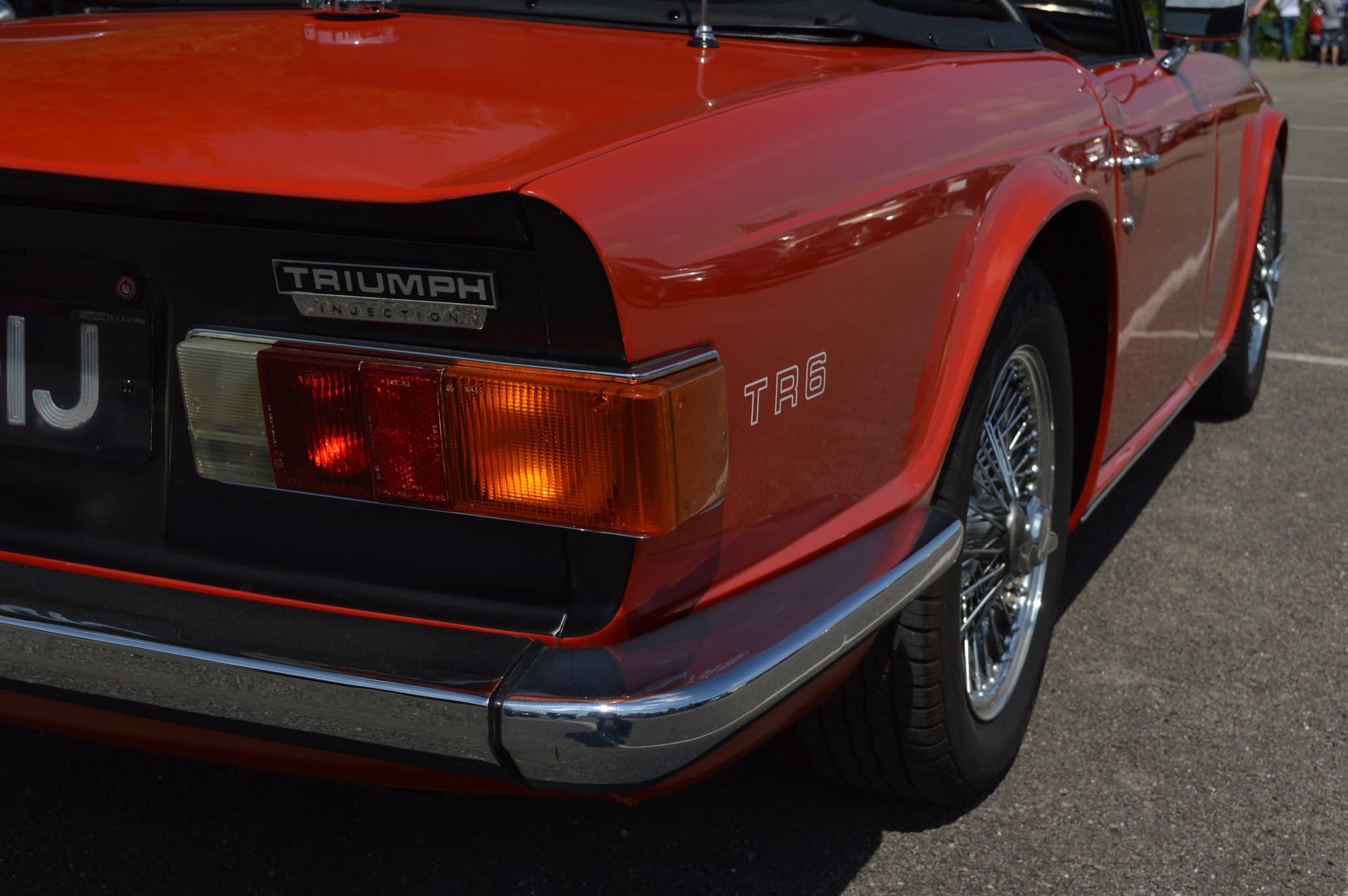 The tail of a red Triumph TR6 with a TRIUMPH badge over the word INJECTION on its black rear panel, a wrap-round tail lamp and a wire wheel.
