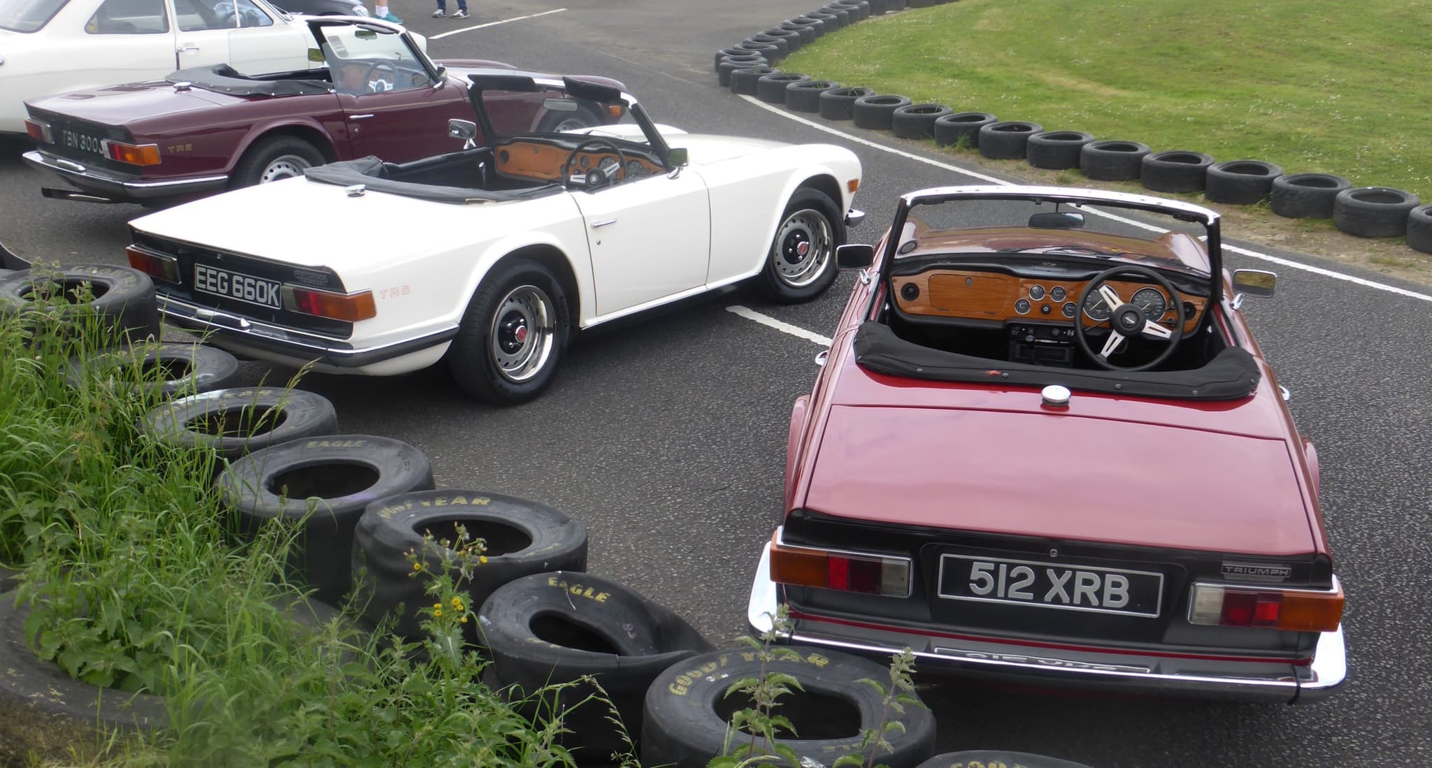 Three Triumph TR6s parked side by side, seen from behind, showing their flat tails and black rear panels.