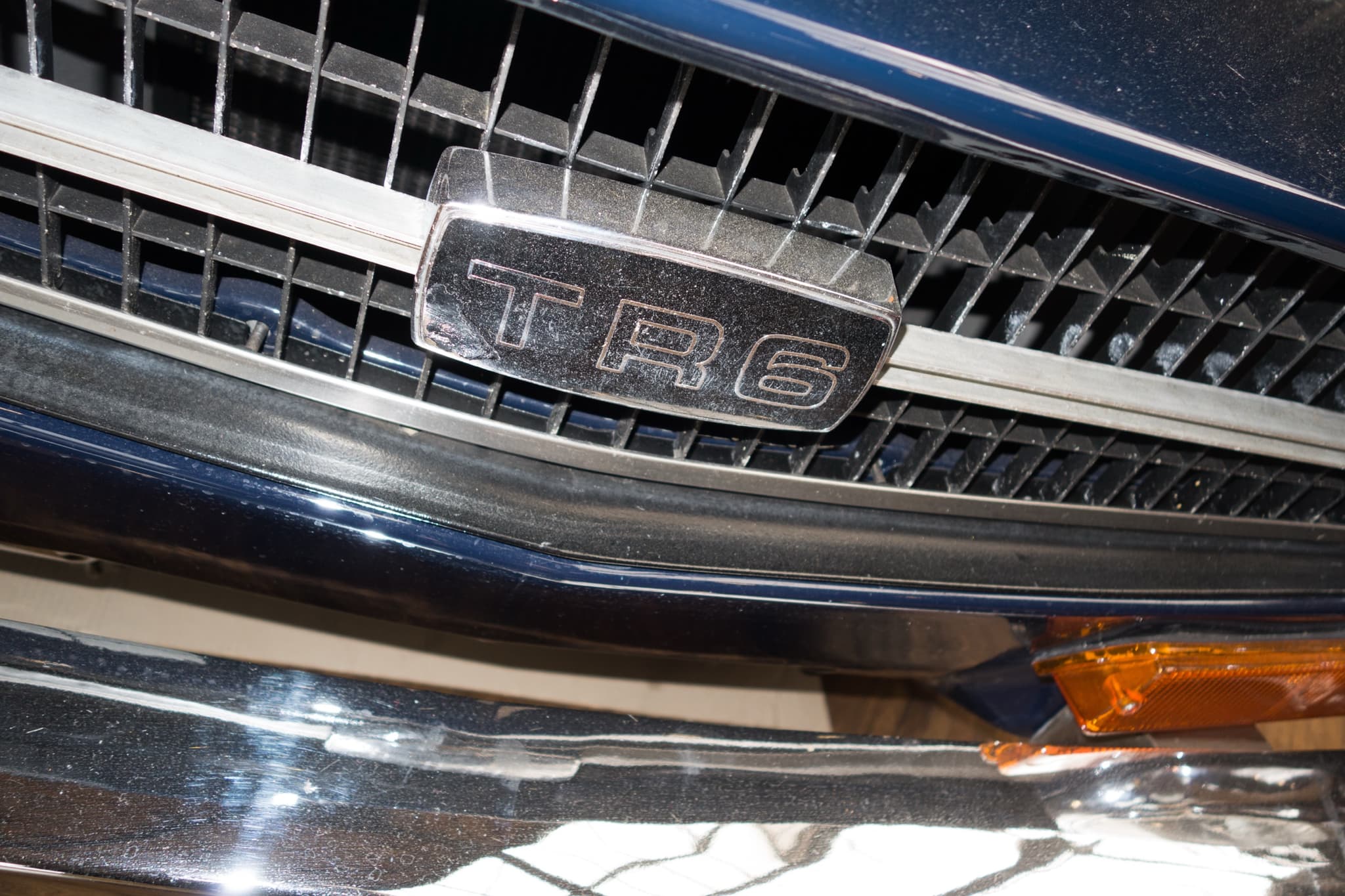 A close view of the chrome TR6 badge on the black grille of a dark blue car.